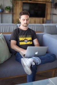 serious-white-man-wearing-a-t-shirt-mockup-working-with-his-laptop-on-a-sofa-a20437